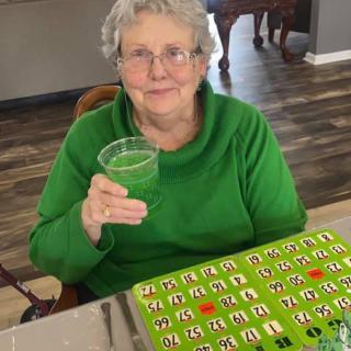 An elderly woman enjoys a green drink while playing bingo.