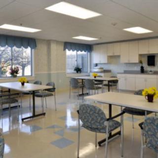 A modern dining area with tables and chairs, featuring bright lighting and a kitchenette.