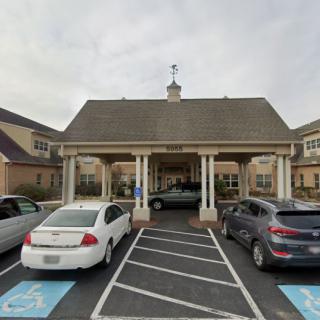 A building entrance with a canopy and parked cars in the adjacent parking lot, featuring marked handicap spaces.
