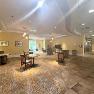 A well-lit interior room with tables and chairs, adorned with artwork and carpeted flooring.