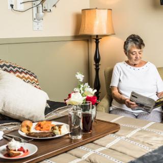 A senior woman enjoys a peaceful moment reading in a cozy living room setting, accompanied by a delicious meal on the table.