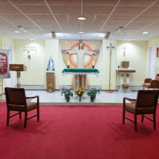 A chapel with an altar and crucifix, featuring red carpet and seating arrangements.