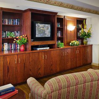 A cozy living room with a wooden cabinet and bookshelves, featuring a television and floral decorations.