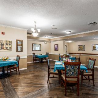 A well-lit dining room with neatly arranged tables and chairs, featuring warm decor and hardwood flooring.
