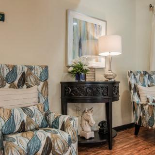 A cozy living room with patterned armchairs, a round table, and a lamp providing ambient lighting.