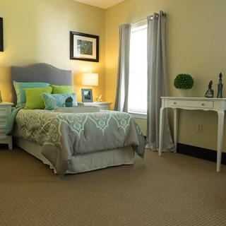 A cozy bedroom with a neatly arranged bed, soft lighting, and a small desk by the window.