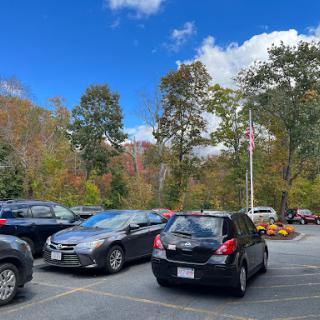 A view of a parking lot surrounded by trees in autumn foliage under a partly cloudy sky.
