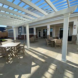 A sunny patio area featuring a pergola with tables and chairs arranged for outdoor seating.