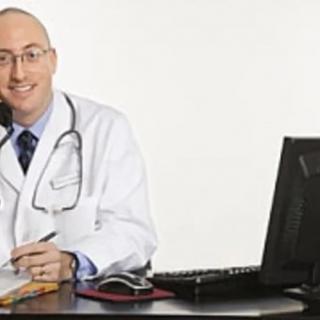 A doctor sitting at a desk with a computer and notepad.