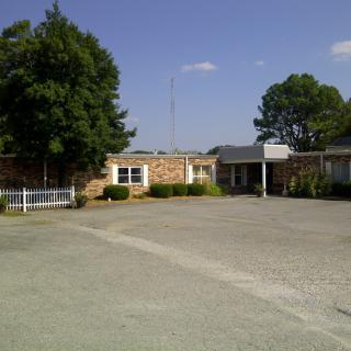 A view of a building with a parking lot in the foreground and trees under a clear blue sky.