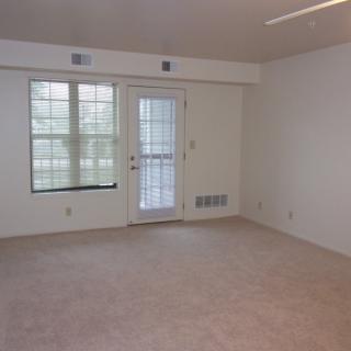 A vacant carpeted room with large windows and a door.