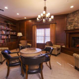 A cozy library room with wooden shelves, a fireplace, and a round table surrounded by armchairs.