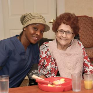 A caregiver spending time with an elderly woman during mealtime.