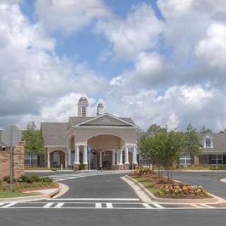An elegant building with a grand entrance, surrounded by well-maintained landscaping under a cloudy sky.