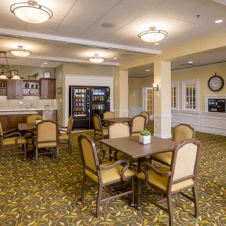 A cozy dining area with tables and chairs, featuring warm lighting and a patterned carpet.