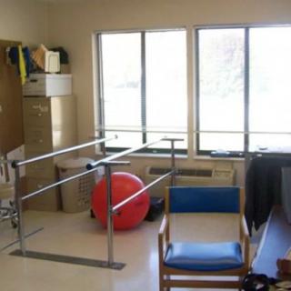 A physical therapy room equipped with parallel bars and a fitness ball.
