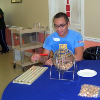 A person playing bingo, seated at a table with a bingo cage and numbers.