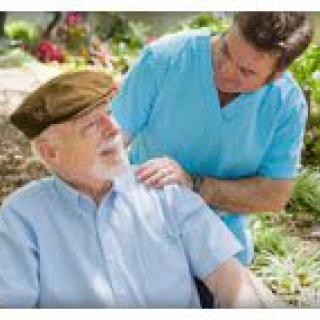 A caregiver attentively engaging with an elderly man in a wheelchair outdoors.