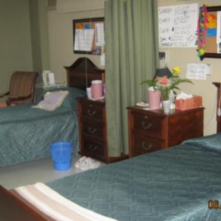 A hospital room with two beds separated by a curtain, featuring medical equipment and furniture.