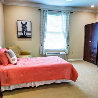 A cozy bedroom featuring a single bed with a coral bedspread, a framed artwork on the wall, and a window with curtains allowing natural light to fill the room.
