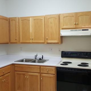 A modern kitchen with wooden cabinets, electric stove, and a double sink.