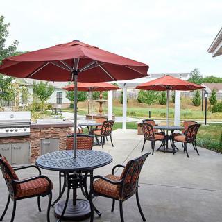 An outdoor patio area with tables, chairs, and red umbrellas in a garden setting.