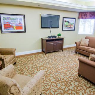 A cozy living room featuring a sofa, armchairs, a television, and framed artwork on the walls.