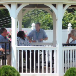 A group of people engaged in conversation under a gazebo on a sunny day.
