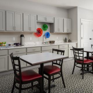 A modern kitchen with a dining area featuring red cushioned chairs and a small table, complemented by neutral cabinets and colorful wall decorations.