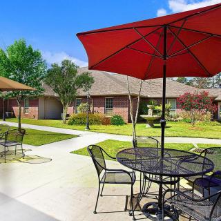 A sunny outdoor patio area with tables, chairs, and umbrellas set against a landscaped garden.