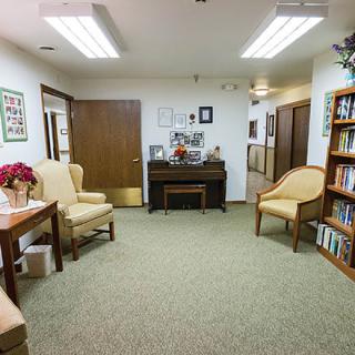 A neatly organized waiting room with comfortable chairs, a piano, and bookshelves.