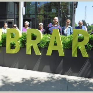 Group of people standing behind large 'LIBRARY' sign outside a building.