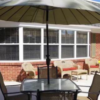 A cozy patio area with a table, chairs, and an umbrella set against a brick house with large windows.
