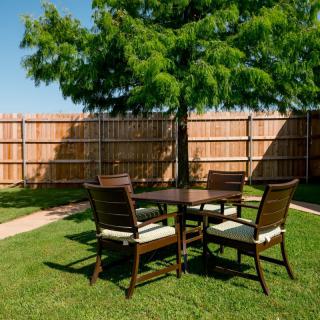 A set of outdoor furniture on a grassy backyard with a tree and wooden fence.