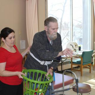 A caregiver assists an elderly man using a walker in a rehabilitation setting.