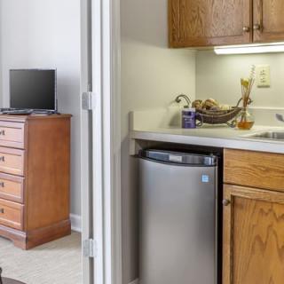 A cozy apartment kitchen with wooden cabinets, a mini-fridge, and adjacent living space with a TV.