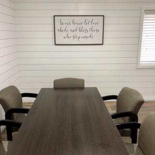 A simple conference room with a long meeting table and chairs, featuring wall art on a shiplap wall.