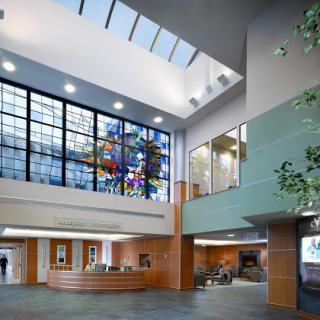 A spacious and modern lobby featuring large windows that allow natural light to flood the space, complemented by a vibrant stained glass window and contemporary furnishings.