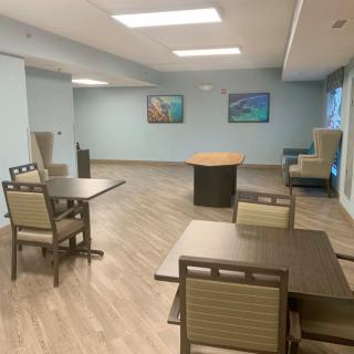 A modern, spacious room with tables and chairs, featuring a wooden floor and contemporary lighting.