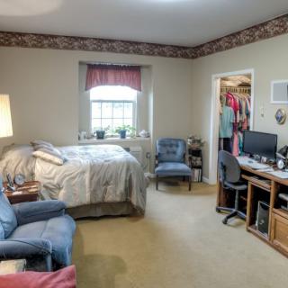 A cozy bedroom featuring a bed, desk, and seating area with a window and closet.