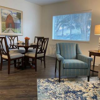 A cozy corner featuring a dining table set, an armchair, and a side table with a lamp in a well-lit living space.