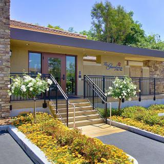A modern building entrance features well-maintained landscaping and elegant stone accents.
