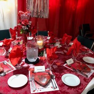 A beautifully decorated dining table with a red theme, featuring elegant table settings and a floral centerpiece.