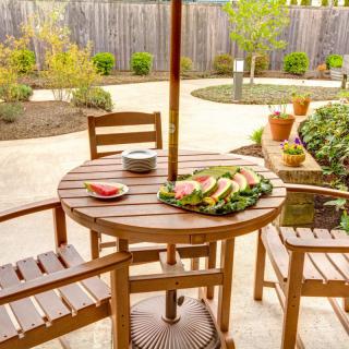 A cozy backyard patio with a wooden table set for a meal, surrounded by plants.