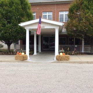 A building entrance decorated with hay bales and pumpkins, featuring an American flag.