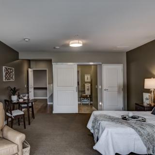 A modern bedroom with stylish furnishings, including a bed, chair, table, and lamp.