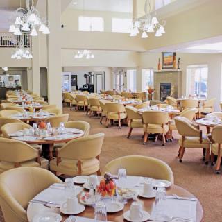 A spacious dining hall with neatly arranged tables and chairs, illuminated by elegant chandeliers.