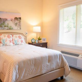 A cozy bedroom with a neatly made bed, a bedside lamp, and a large window.