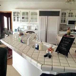 A spacious kitchen with white tiled countertops and cabinets, featuring a central island adorned with decorative items and a small chalkboard.