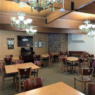 An empty dining area with wooden tables, chairs, and chandeliers.